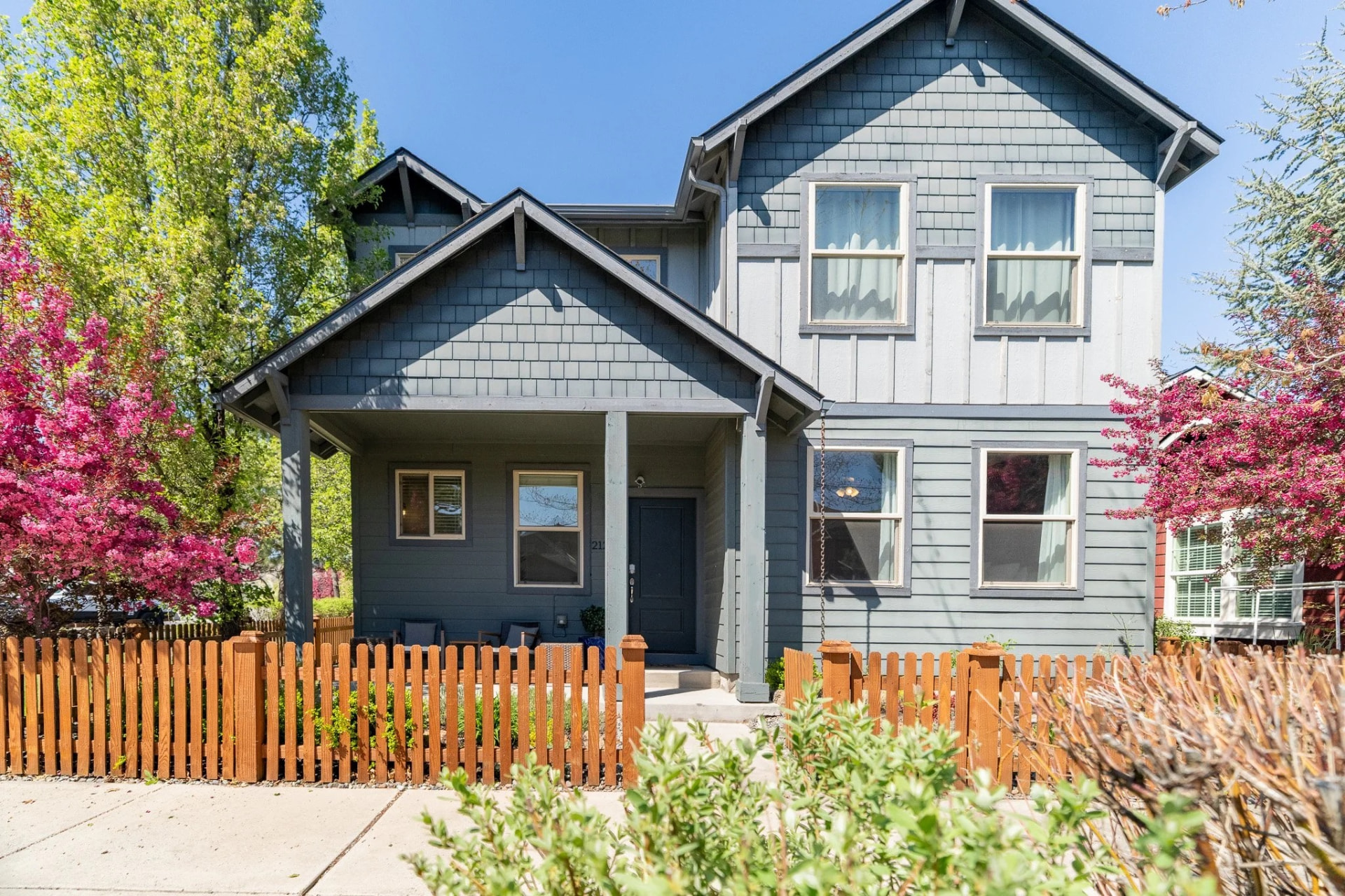 Bellflower House, a blue two-story craftsman home with a covered front porch and picket fence